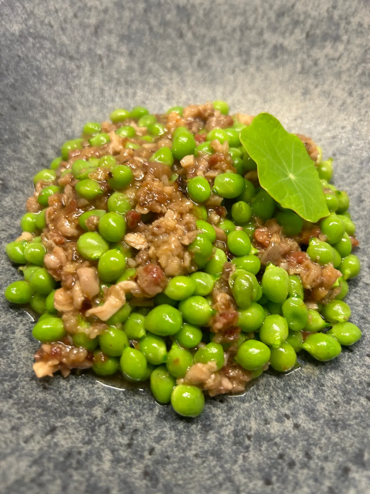 Sautéed seasonal peas with picada and a nasturtium flower