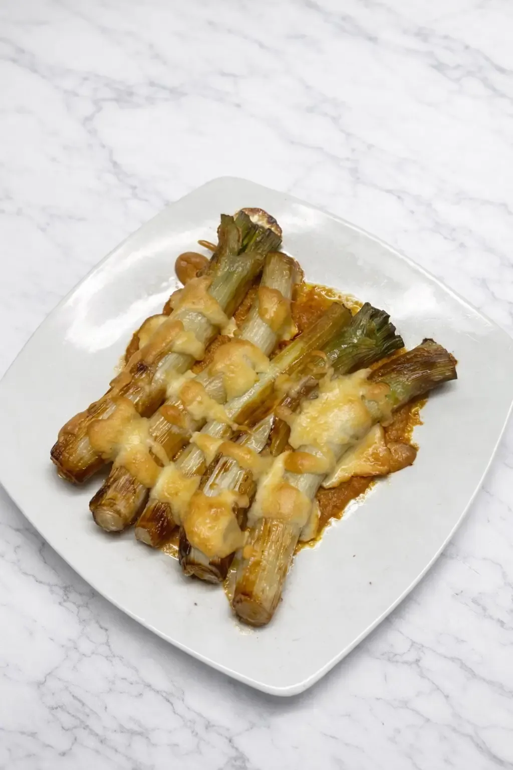 Roasted leeks au gratin on a sauce, on a white plate, from the kitchen at La Estrella 1924